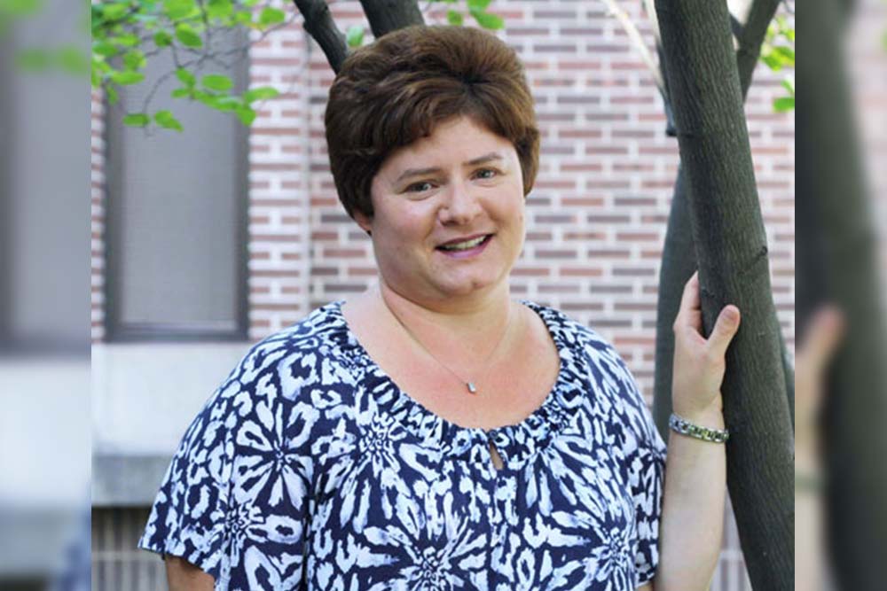 headshot of a woman wearing a necklace and a blue and white shrit